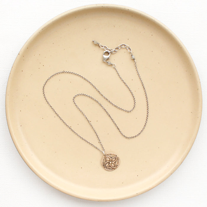 The bronze wanderer coin necklace styled on a tan plate to show the adjustable lobster clasp closure