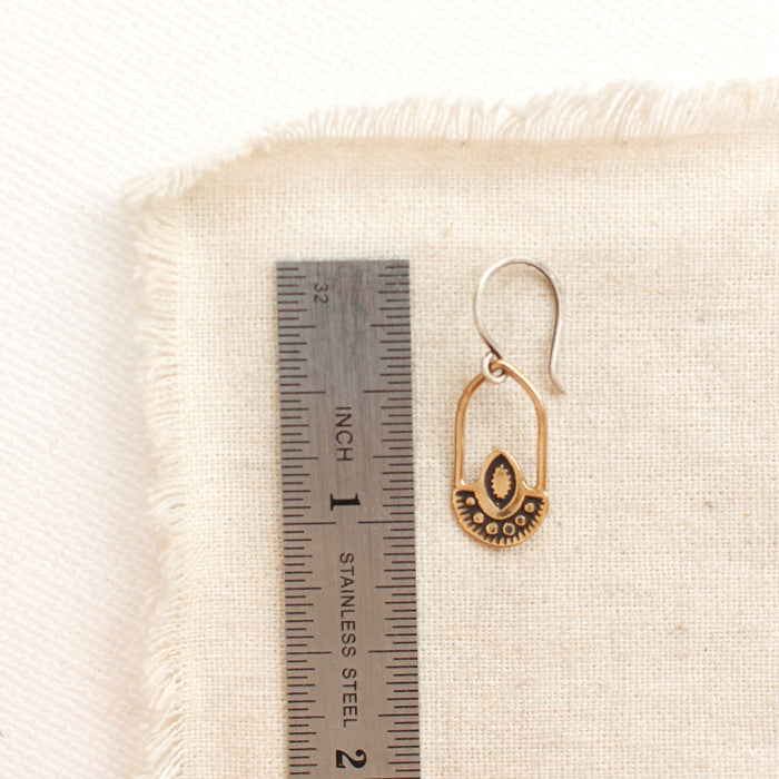 A bronze wanderer hoop earring next to a ruler for size reference