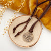 The bronze wanderer medallion leather necklace styled on wood with yellow velvet and dried grass