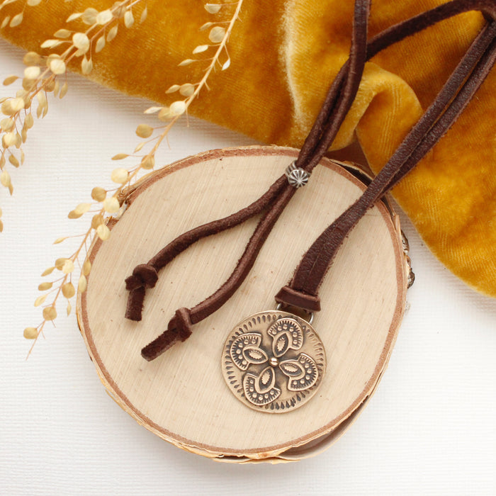 The bronze wanderer medallion leather necklace styled on wood with yellow velvet and dried grass
