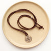 The bronze wanderer medallion leather necklace styled on a tan plate to show the adjustable silver slider
