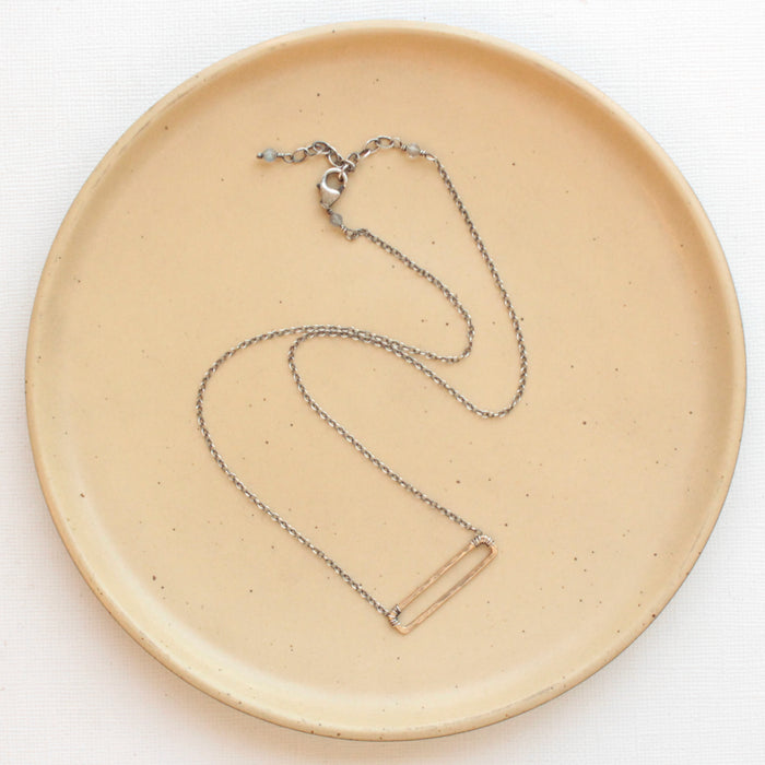 The bronze open bar necklace styled on a tan plate to show the adjustable lobster clasp closure