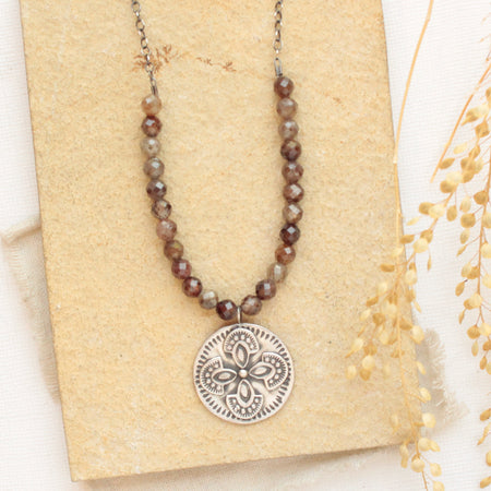 The brown zircon wanderer medallion necklace styled on a tan rock with dried grass