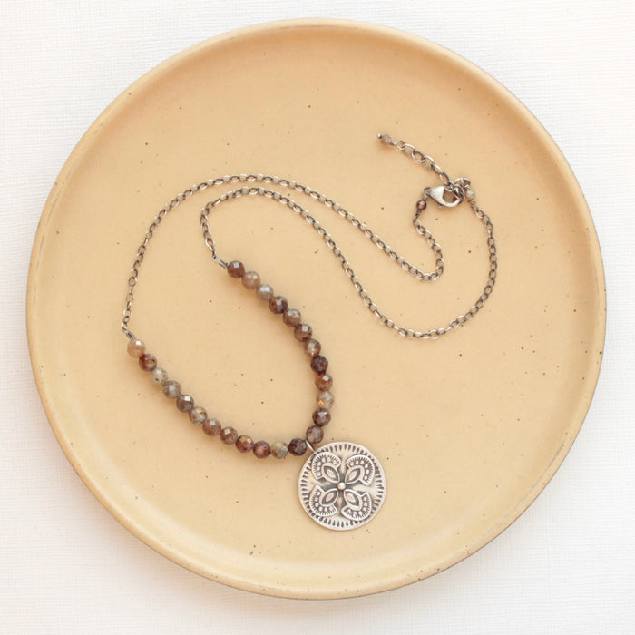 The brown zircon wanderer medallion necklace styled on a tan plate to show the adjustable lobster clasp closure
