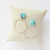 The carved turquoise flower post hoop earrings styled on a linen pillow