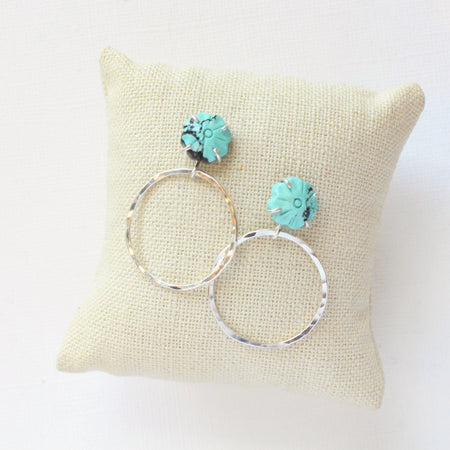 The carved turquoise flower post hoop earrings styled on a linen pillow