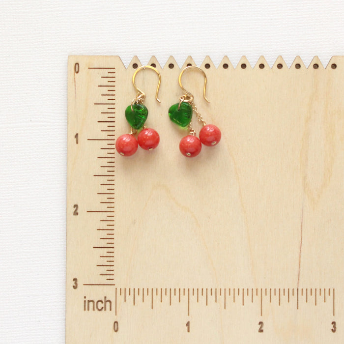 The little cherry earrings on a wooden ruler for size reference. 