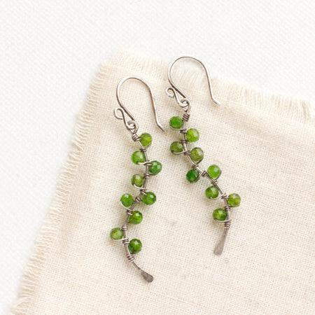 The chrome diopside wrapped silver vine earrings styled on tan linen