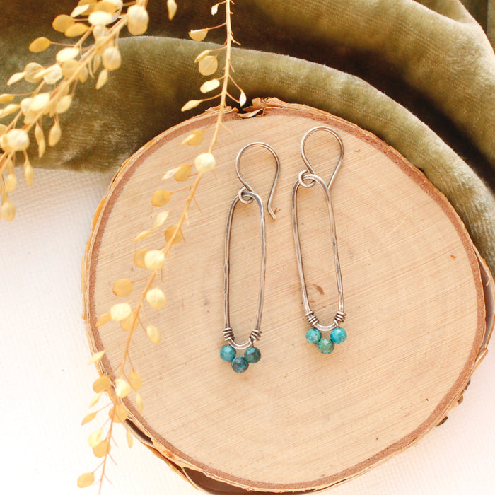 The chrysocolla wrapped long hoop earrings styled on wood with green velvet and dried grass