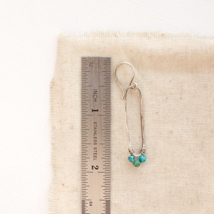 A chrysocolla wrapped long hoop earring next to a ruler for size reference