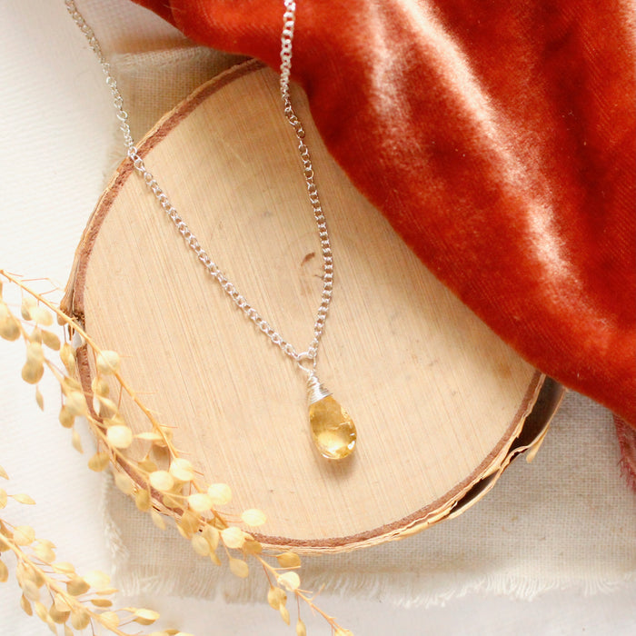 The citrine drop silver necklace styled on wood with orange velvet and dried grass