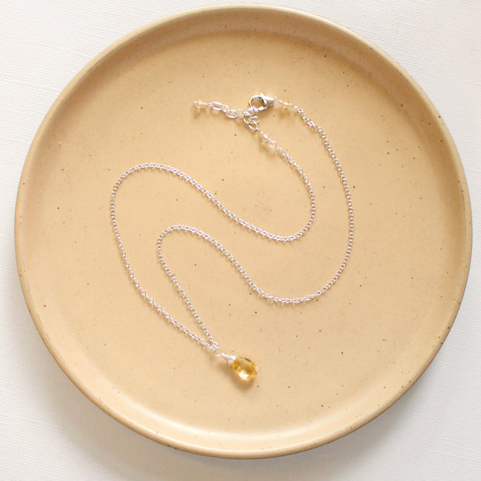 A citrine drop necklace styled on a tan plate to show the adjustable lobster clasp closure