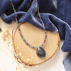 The cleo sapphire necklace styled on wood with blue velvet and dried grass
