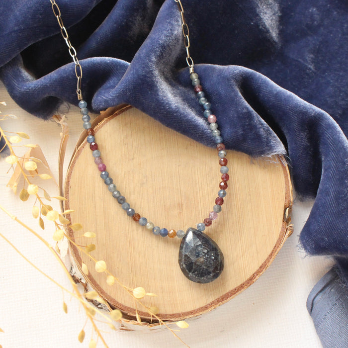 The cleo sapphire necklace styled on wood with blue velvet and dried grass