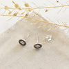 The stamped silver clover post earrings styled on tan linen with dried grass