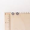 The stamped silver clover post earrings on a wooden ruler for size reference