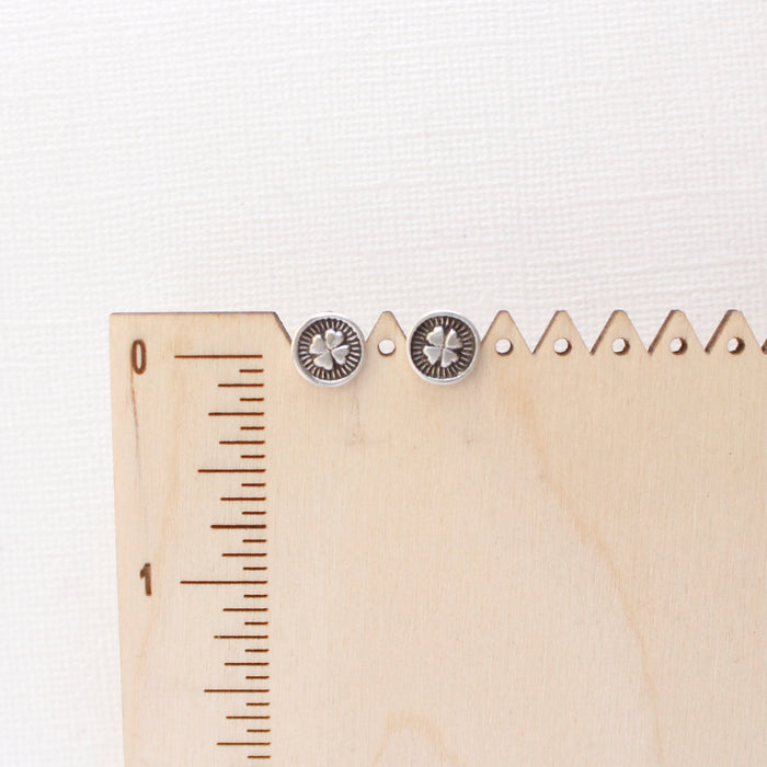 The stamped silver clover post earrings on a wooden ruler for size reference