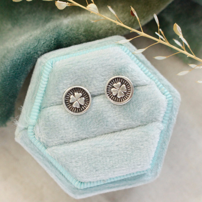 The stamped silver clover post earrings styled on a blue velvet box with green velvet and dried grass