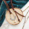 The columbine hoop pearl adjustable leather necklace styled on wood with blue velvet and dried grass