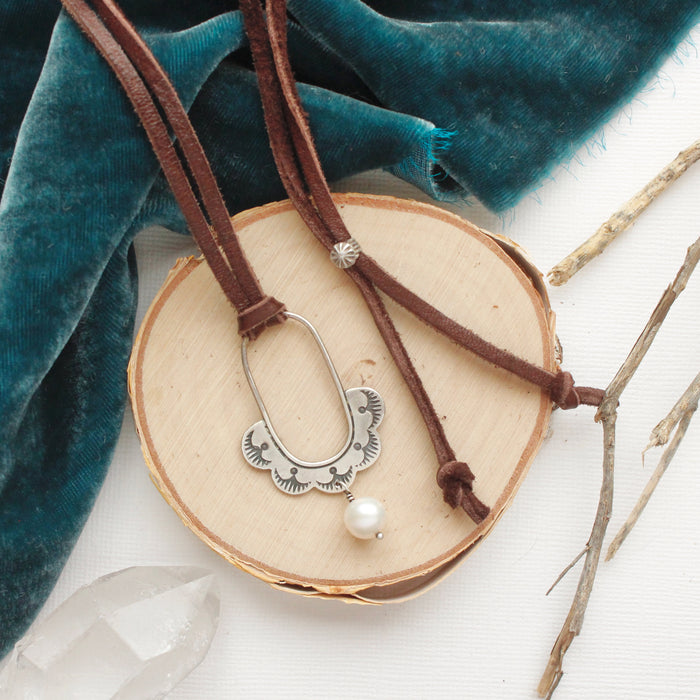 The columbine hoop pearl adjustable leather necklace styled on wood with blue velvet and dried grass