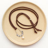 The columbine hoop pearl adjustable leather necklace styled on a tan plate to show the entire leather strap and silver slider