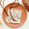 The columbine hoop pearl adjustable leather necklace styled on an orange plate with the matching earrings