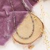 The dainty sapphire necklace styled on wood with purple velvet and dried grass