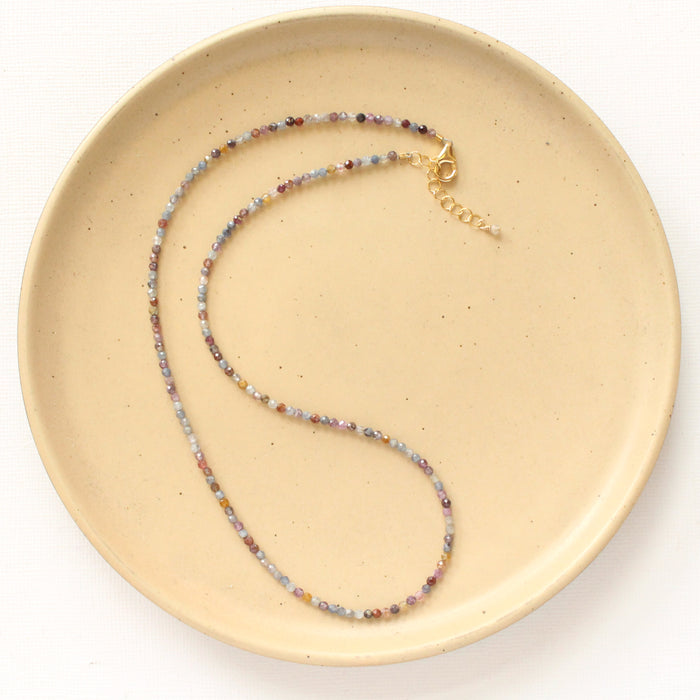 The dainty sapphire necklace styled on a tan plate to show the adjustable lobster clasp closure