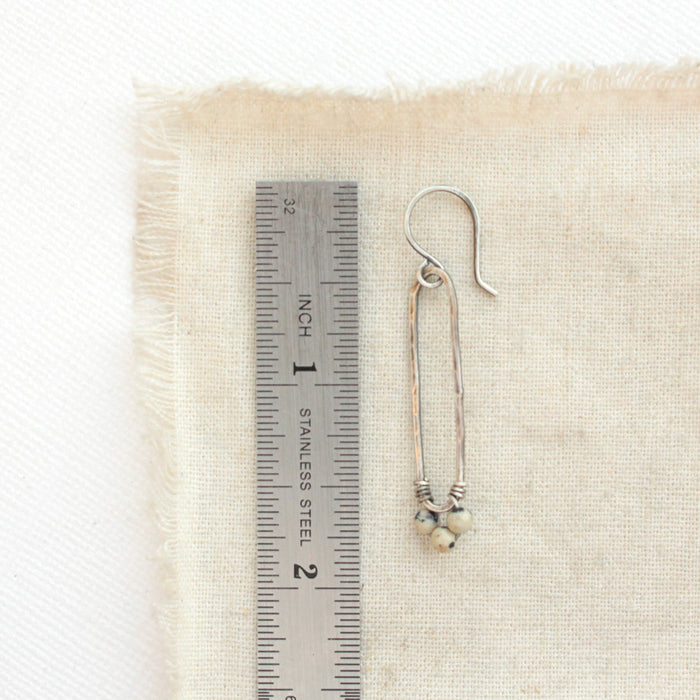 A dalmatian jasper forged long hoop earrning styled next to a ruler for size reference