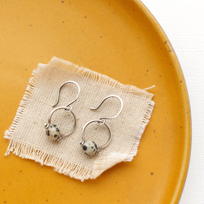 The dalmatian jasper la cloche earrings styled on a yellow plate with tan linen