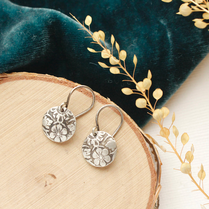 The embossed siena disc earrings styled on wood with blue velvet and dried grass