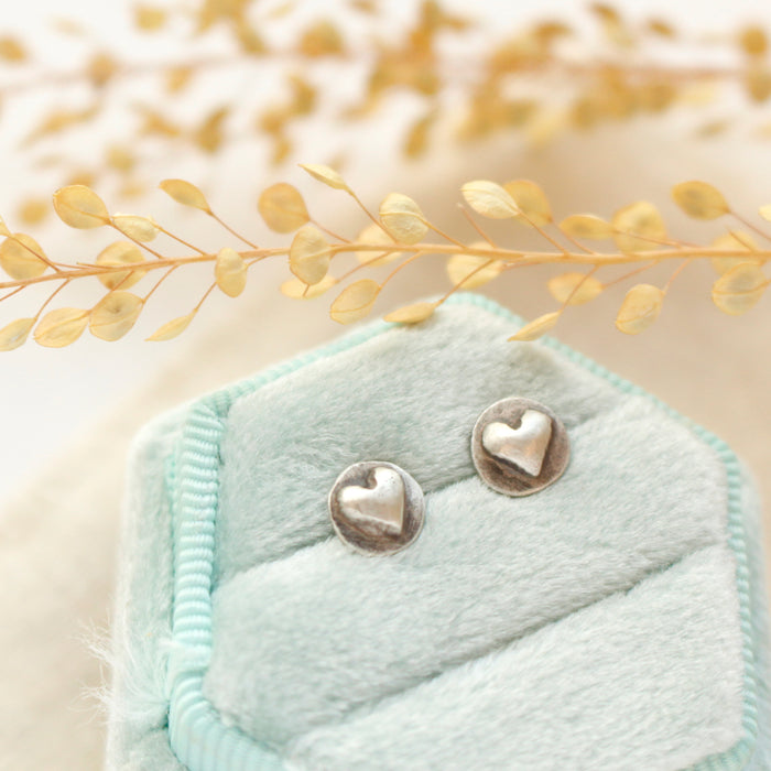 The silver heart post earrings styled on a blue velvet box with linen and dried grass
