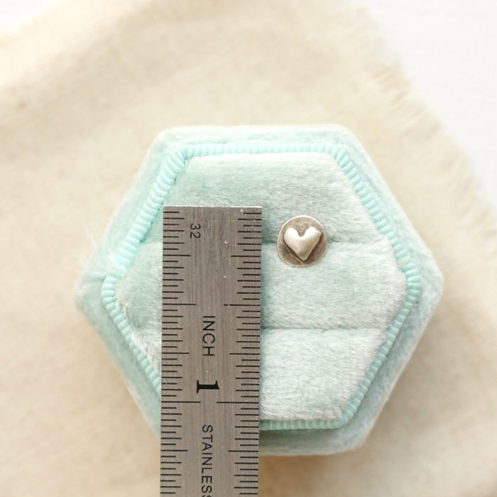 A silver heart post earring next to a ruler for size reference