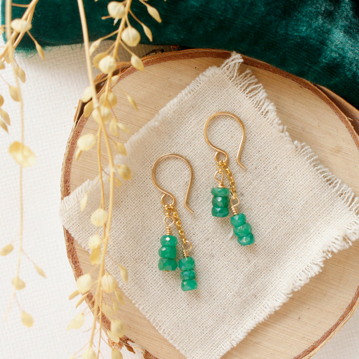 The emerald dangle earrings styled on wood with green velvet and dried grass