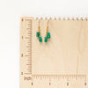 The emerald dangle earrings on a wooden ruler for size reference