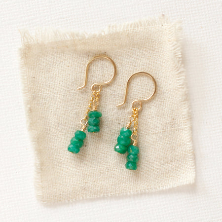 The emerald dangle earrings styled on tan linen