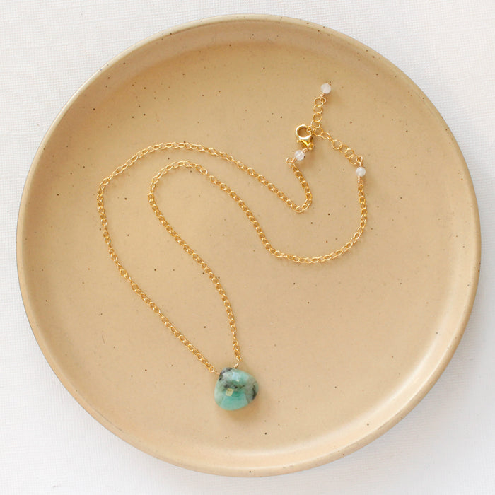The emerald drop gold necklace styled on a tan plate to show the adjustable lobster clasp closure