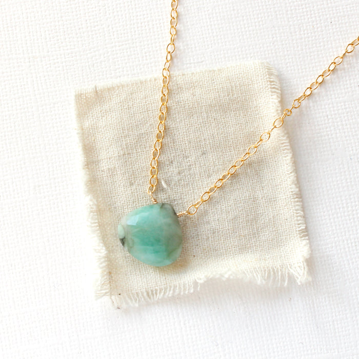 The emerald drop gold necklace styled on tan linen