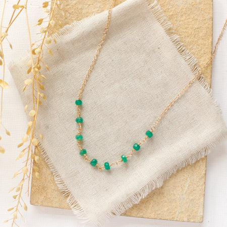 The emerald collar necklace styled on a tan rock with linen and dried grass