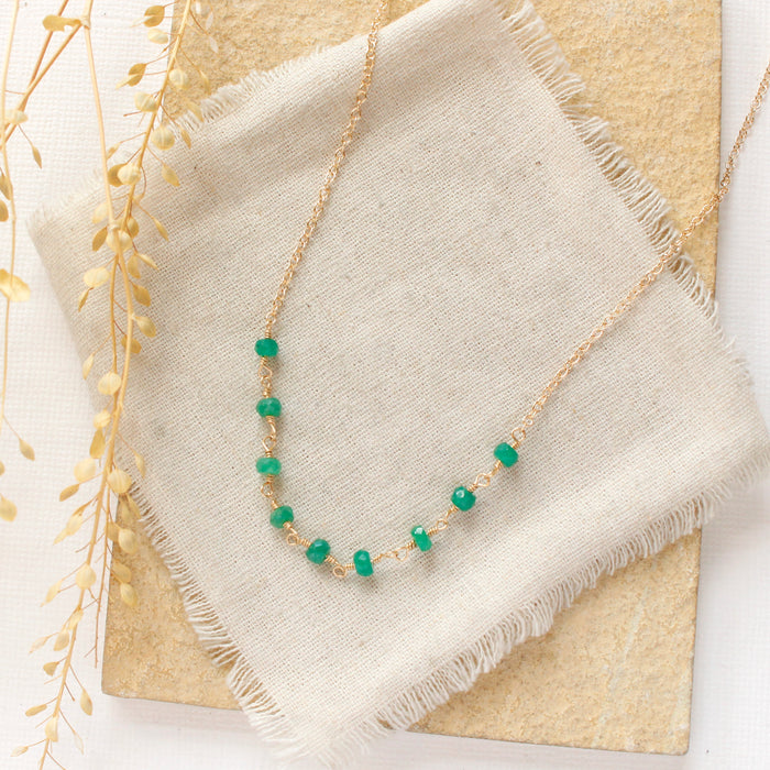 The emerald collar necklace styled on a tan rock with linen and dried grass