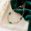The emerald paperclip bracelet styled on tan linen with green velvet and dried grass