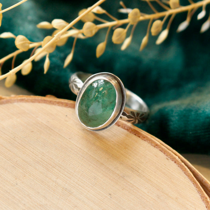 The emerald and stamped rays ring styled on wood with green velvet and dried grass