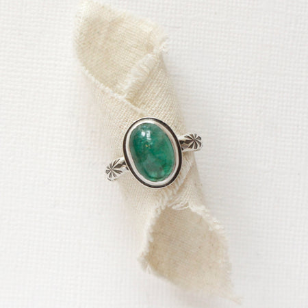 The emerald and stamped rays ring styled on rolled tan linen