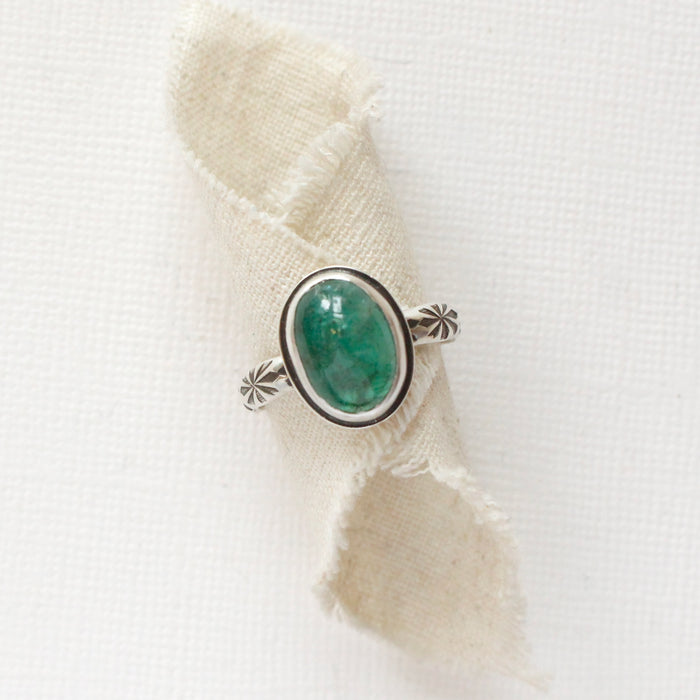 The emerald and stamped rays ring styled on rolled tan linen