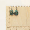 The prong set emerald earrings on a wooden ruler for size reference