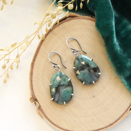 The prong set emerald earrings styled on wood with green velvet and dried grass