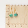 The emerald swing earrings on a wooden ruler for size reference