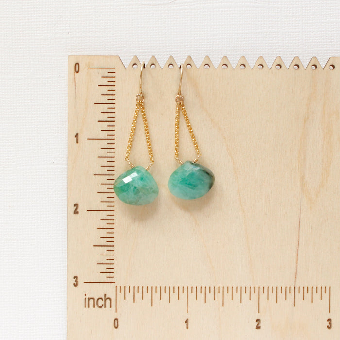 The emerald swing earrings on a wooden ruler for size reference