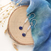 The opal and lapis drop earrings styled on wood with blue velvet and dried grass