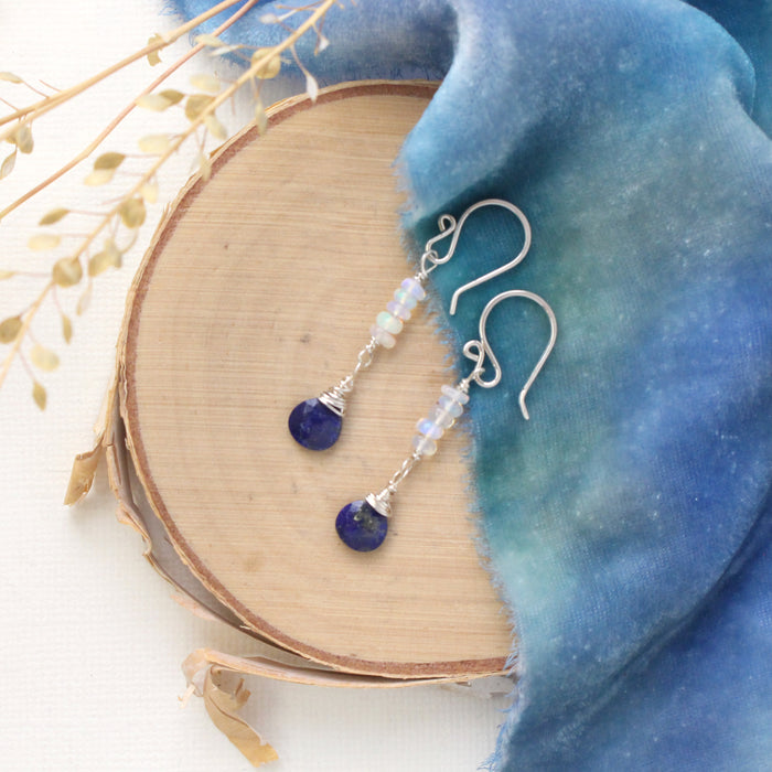 The opal and lapis drop earrings styled on wood with blue velvet and dried grass